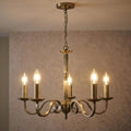 Antique brass five-light chandelier with scroll arms and lit candle bulbs against a patterned background.