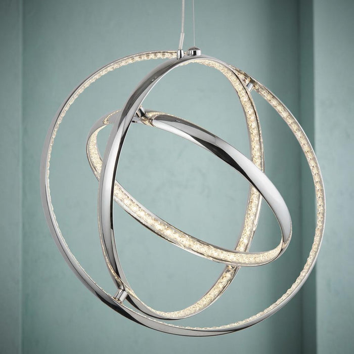 Interlocking chrome and crystal LED rings forming a gyro pendant light against a soft blue wall.