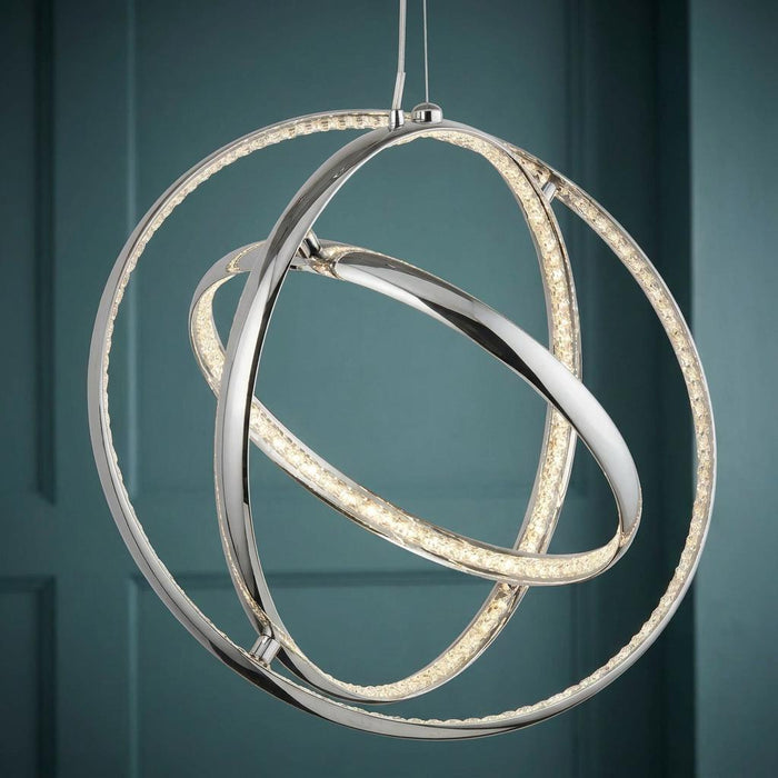 Modern chrome and crystal three-ring gyro LED pendant light hanging against a dark teal paneled wall.