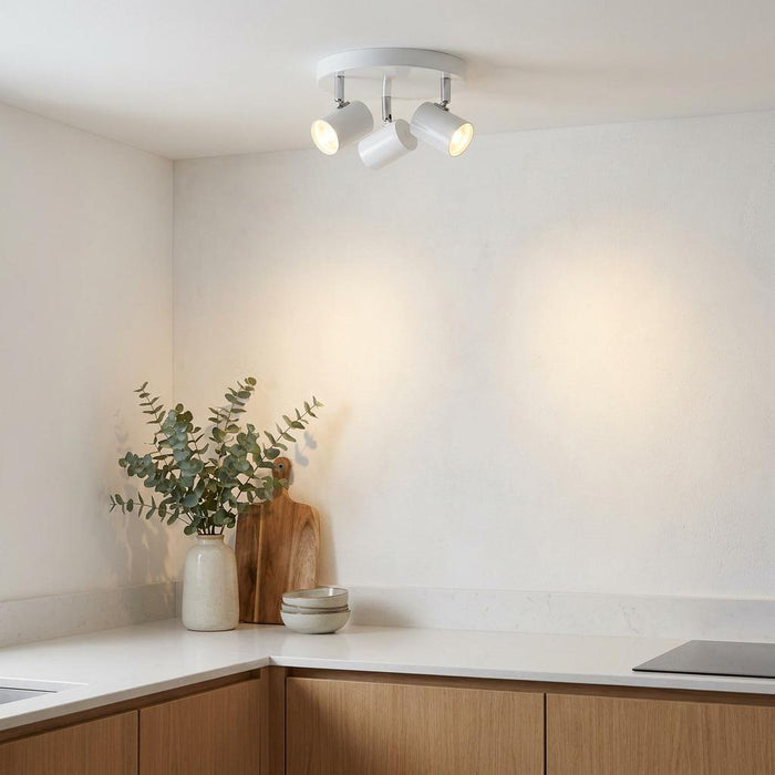 Rollo 3 light white cylinder head flush adjustable spotlight installed on a kitchen ceiling casting light on the wall.