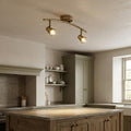 Antique brass twin kitchen spotlight with curved bar and adjustable heads illuminating a rustic wooden island.