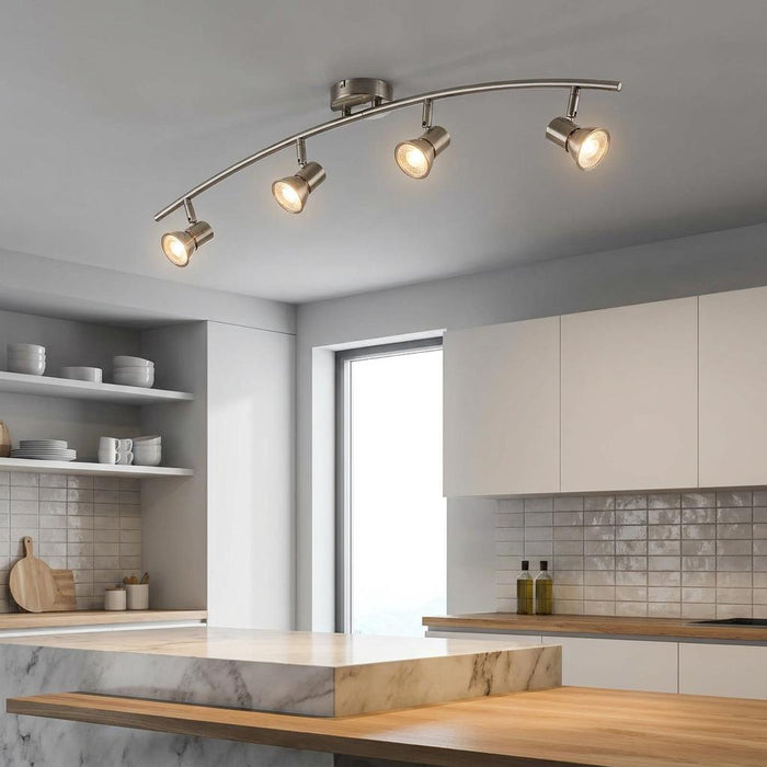 Four-light antique chrome curved spotlight bar illuminating a modern white kitchen with marble countertops.