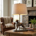 Bronze dog-themed table lamp with a linen shade atop a wooden side table in a rustic living room.