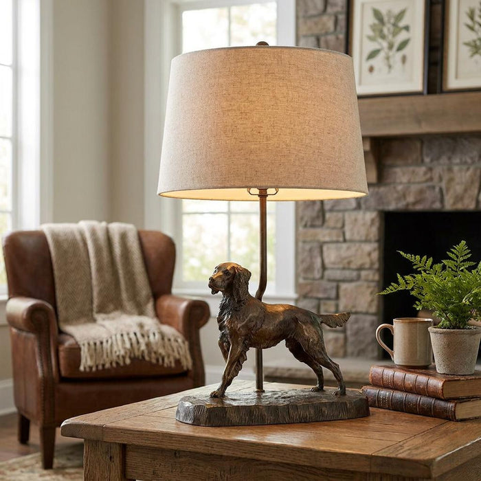 Bronze dog-themed table lamp with a linen shade atop a wooden side table in a rustic living room.