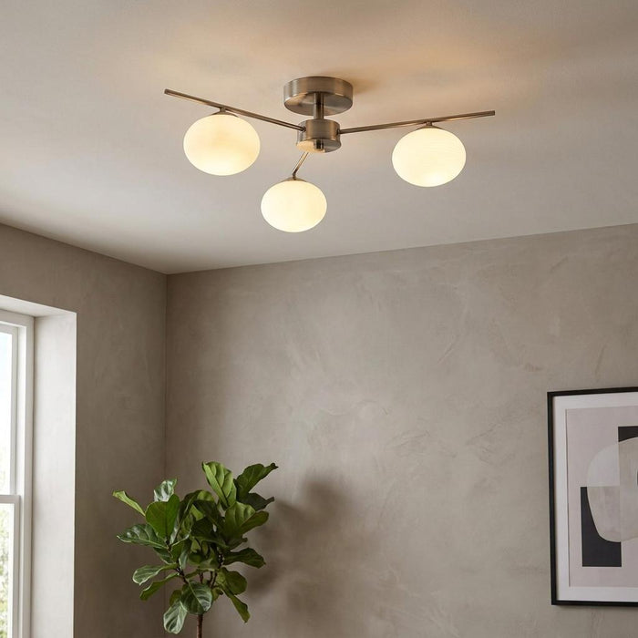 Three opal glass globes on antique chrome arms of a semi-flush ceiling light in a neutral-toned room.