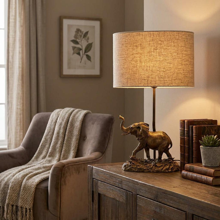 Bronze elephant table lamp with a natural linen shade, placed on a wooden cabinet in a cozy living room.