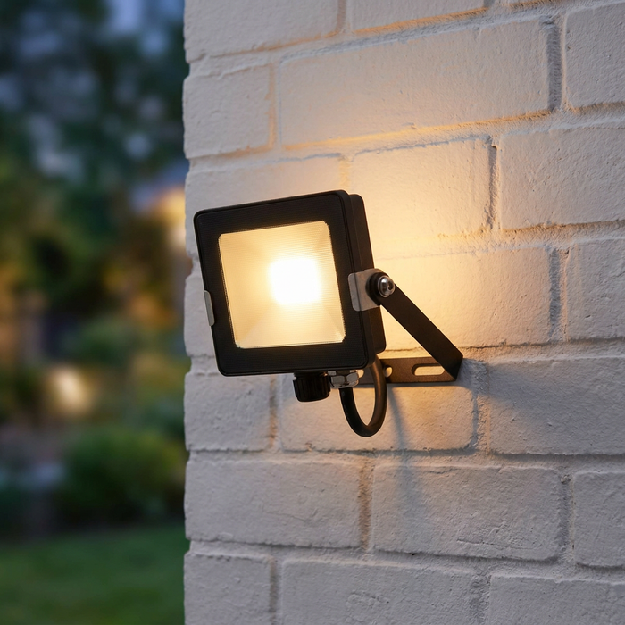 Black square LED floodlight mounted on a white brick wall, illuminated with a warm glow.