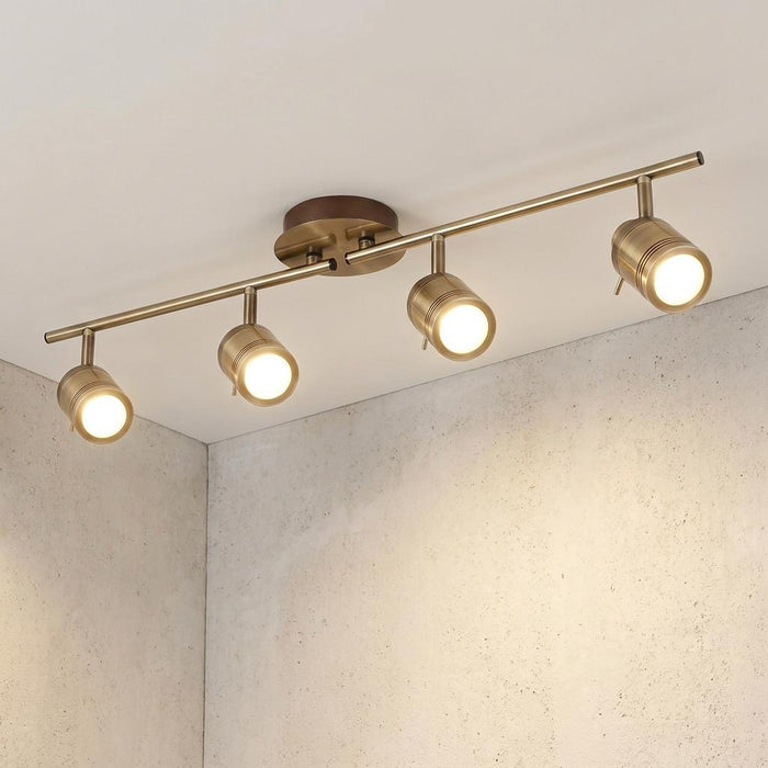 Four-light brass split-bar spotlight with adjustable cylindrical heads mounted on a white ceiling.