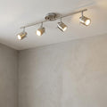 Adjustable four-light silver split-bar spotlight fixture mounted on a white ceiling above a grey textured wall.