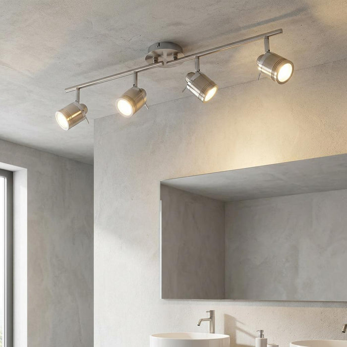 Silver 4-light adjustable split-bar spotlight mounted on a bathroom ceiling, illuminating a mirror and sink area.