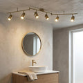 Six-light brass split-bar spotlight mounted on a textured ceiling in a modern bathroom above a round mirror.