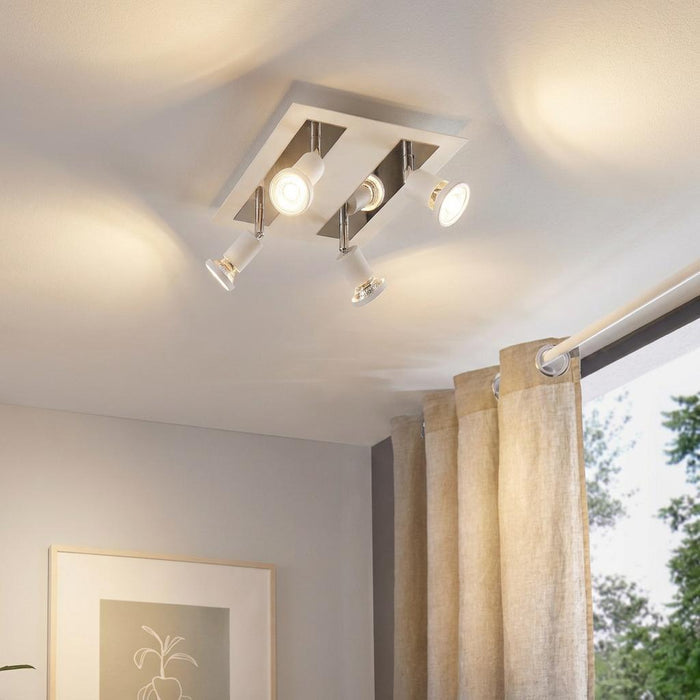 White and chrome 4-light plate spotlight mounted on a ceiling, casting warm light in a modern room.