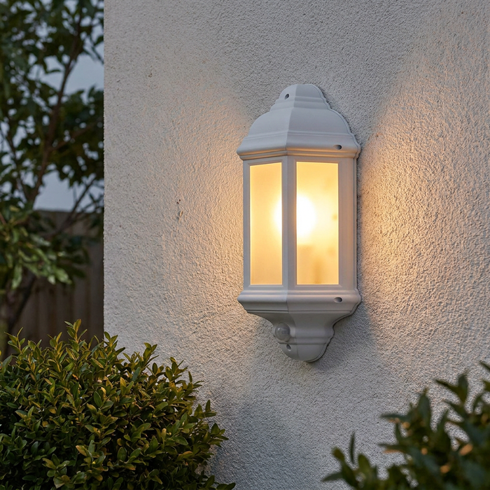 Traditional matt white wall lantern with PIR sensor illuminated on a textured exterior wall.