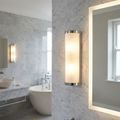 Modern cylindrical chrome and frosted glass bathroom wall light mounted on marble tile.