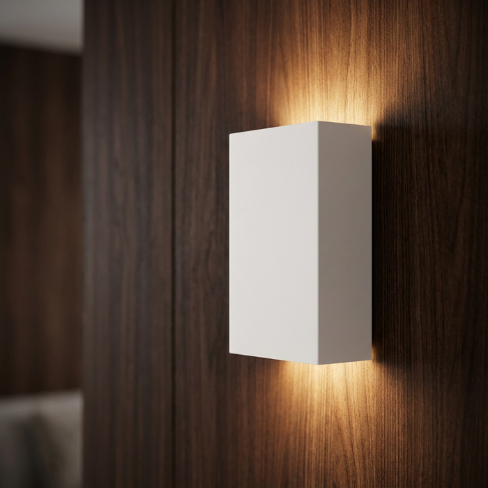 White rectangular plaster wall light on a dark wood wall, casting a warm up-and-down glow.
