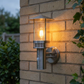 Brushed stainless steel pagoda-style outdoor wall light with a PIR sensor, glowing on a brick wall.