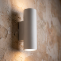 White cylindrical up-and-down plaster wall light emitting a warm glow on a textured stone wall.