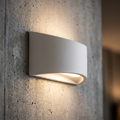 Sleek curved white plaster wall light casting a warm downward glow on a textured concrete wall.
