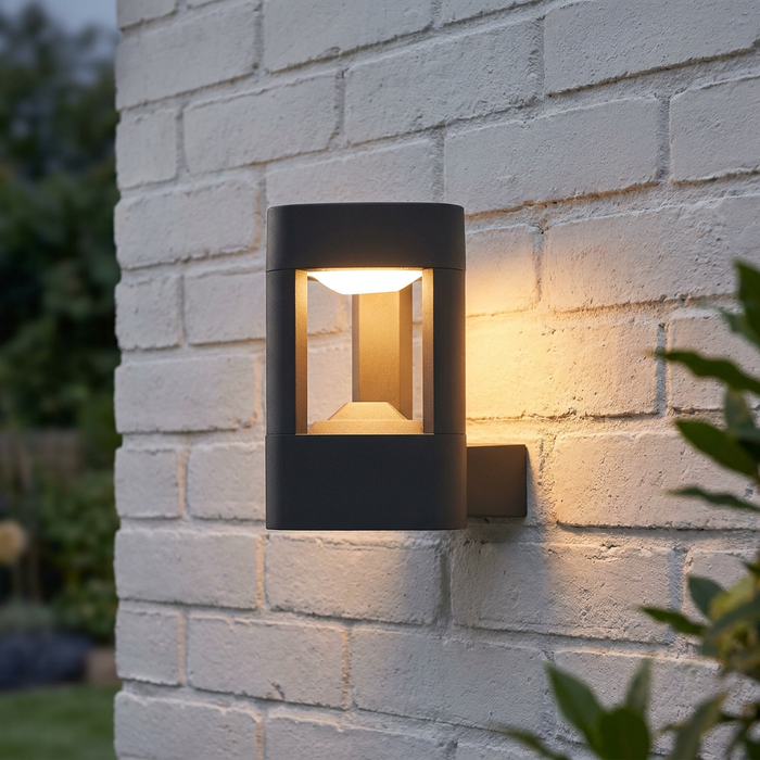Modern grey LED wall light with an open frame mounted on a white brick wall, glowing warmly.