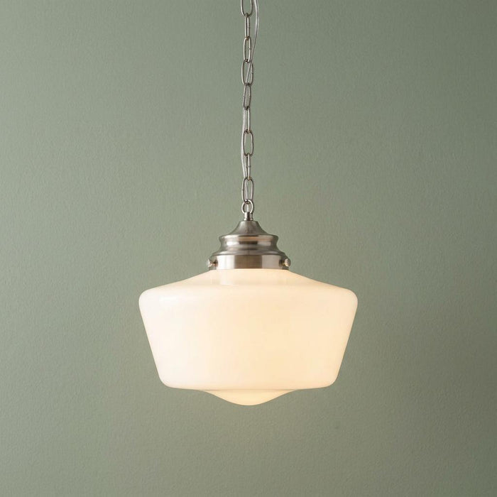 Schoolhouse-style pendant light with a white opal glass shade and chrome chain hanging against a soft green wall.