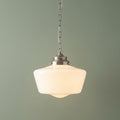 Schoolhouse-style pendant light with a white opal glass shade and chrome chain hanging against a soft green wall.