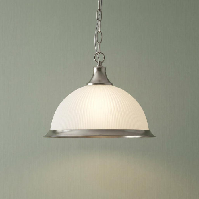 Ribbed white glass dome pendant light with silver metal accents suspended by a chain against a neutral wall.