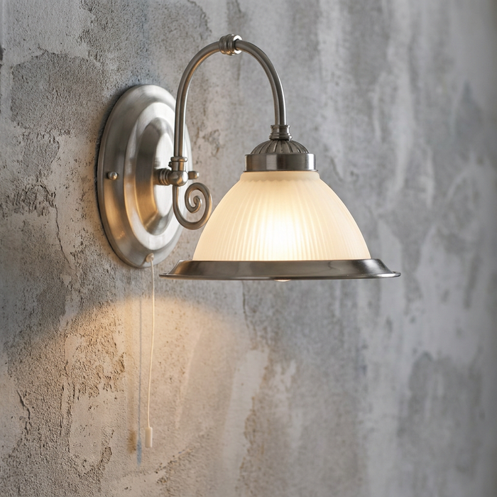 Silver wall sconce with a ribbed glass shade and pull cord, illuminated against a textured grey wall.