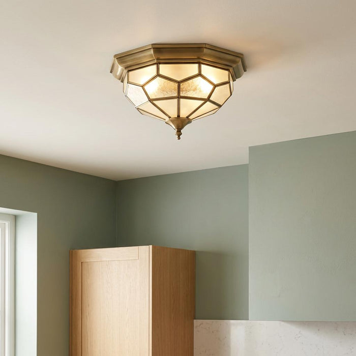 Antique brass and glass flush ceiling light with geometric panels illuminated in a room with green walls.