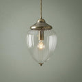 Antique brass ceiling light with a clear ribbed glass acorn shade and a glowing bulb against a green wall.