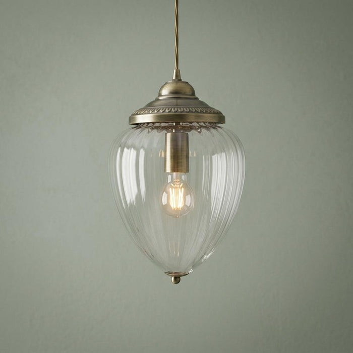 Antique brass ceiling light with a clear ribbed glass acorn shade and a glowing bulb against a green wall.