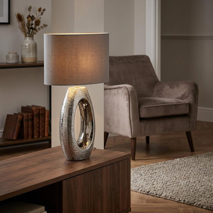 Searchlight Artisan chrome oval table lamp with a grey fabric shade on a wooden sideboard in a living room.