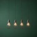 Four industrial pewter wire cage pendant lights with glowing bulbs against a dark green background.