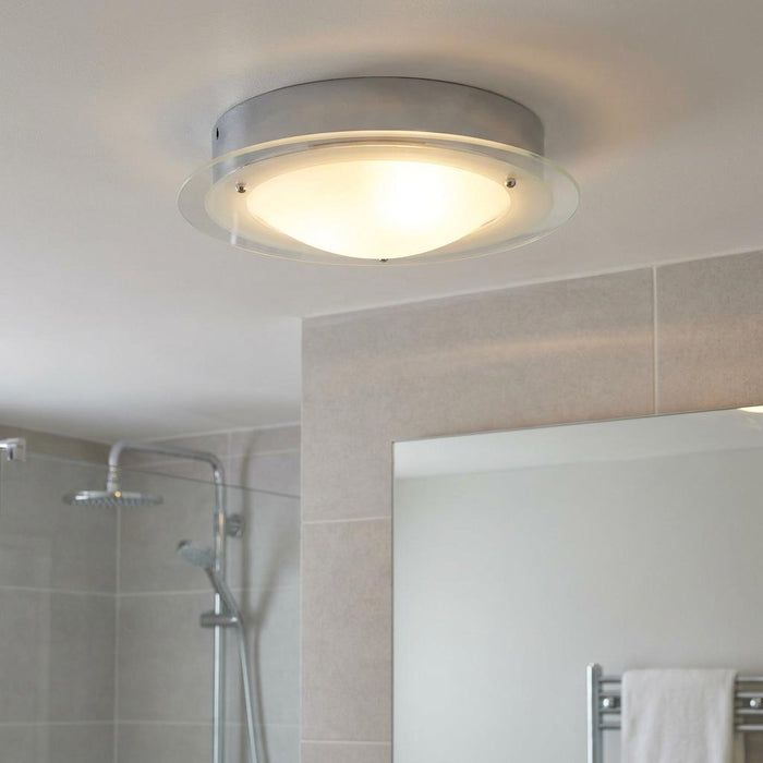 Chrome and glass flush bathroom light mounted on a ceiling above a mirror and shower.