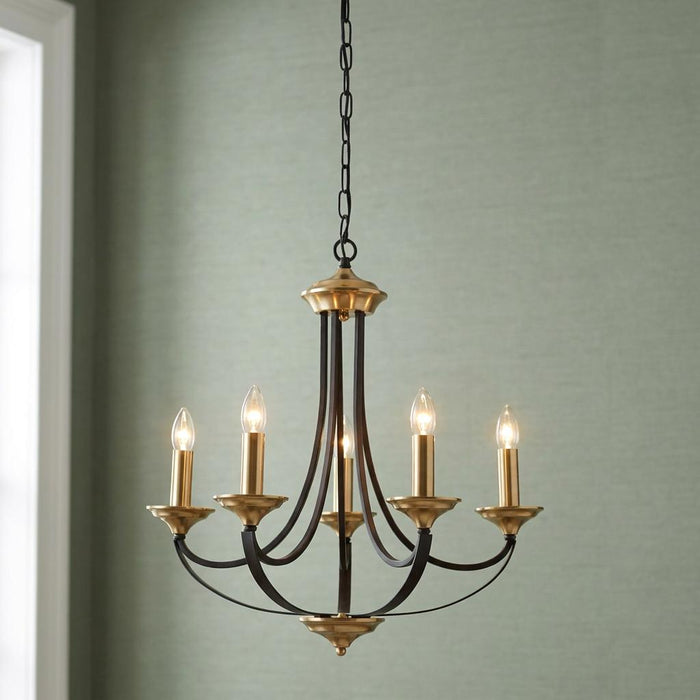 Searchlight Belfry five-light bronze and brass chandelier with candle bulbs against a textured sage green wall.