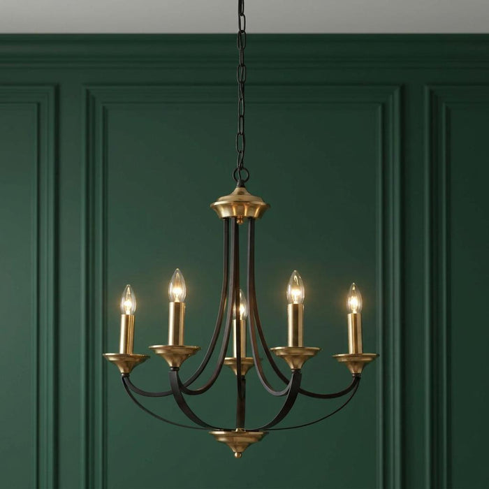 Five-light bronze and brass chandelier with lit candle bulbs against a dark green paneled wall.