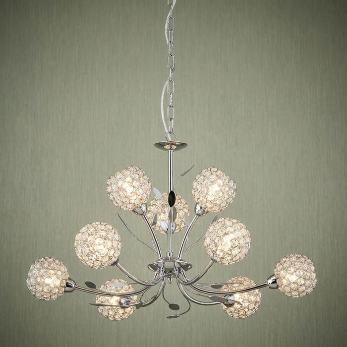 Nine-light chrome chandelier featuring delicate glass crystal ball shades and leaf accents on a green wall.