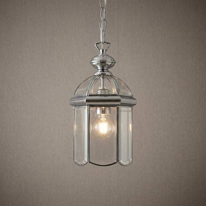 Chrome domed lantern pendant light with bevelled glass panels hanging against a textured grey wall.