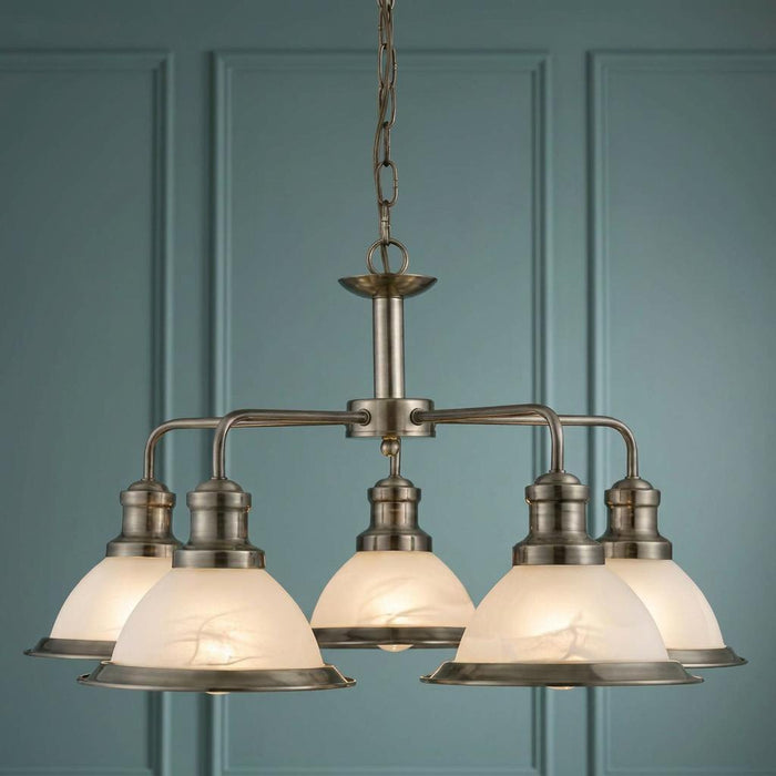 Antique brass five-light ceiling pendant with white marble-effect glass shades against a teal panelled wall.