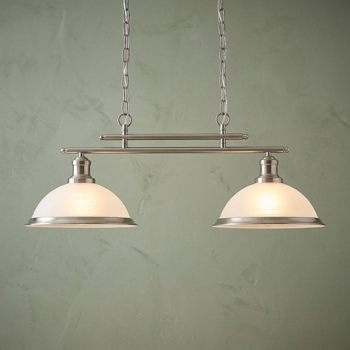 Silver two-light bar pendant with frosted glass dome shades suspended by chains against a sage green wall.