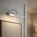 Chrome adjustable picture light casting a warm glow over a framed art piece on a neutral wall.