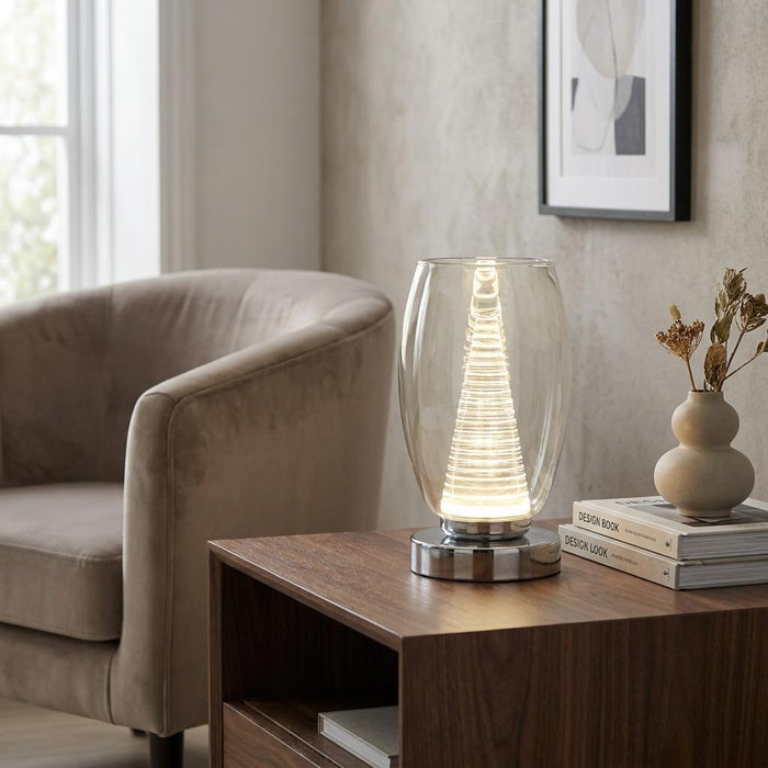 Searchlight Cyclone chrome table lamp with a glass shade and glowing core on a wooden side table.