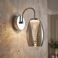 Chrome wall light with a smoked glass oval shade and spiral glowing core, mounted on a textured beige wall.