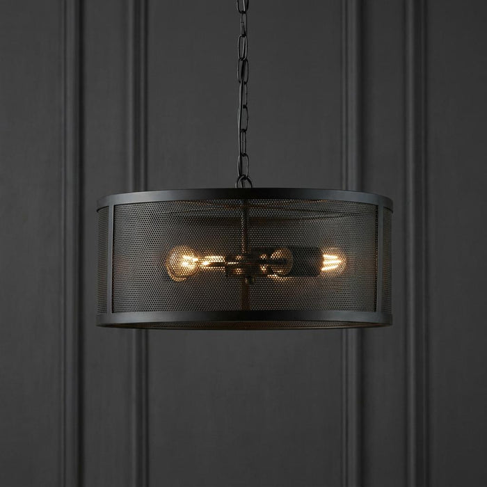 Black mesh drum pendant light with three glowing bulbs against a dark paneled wall.
