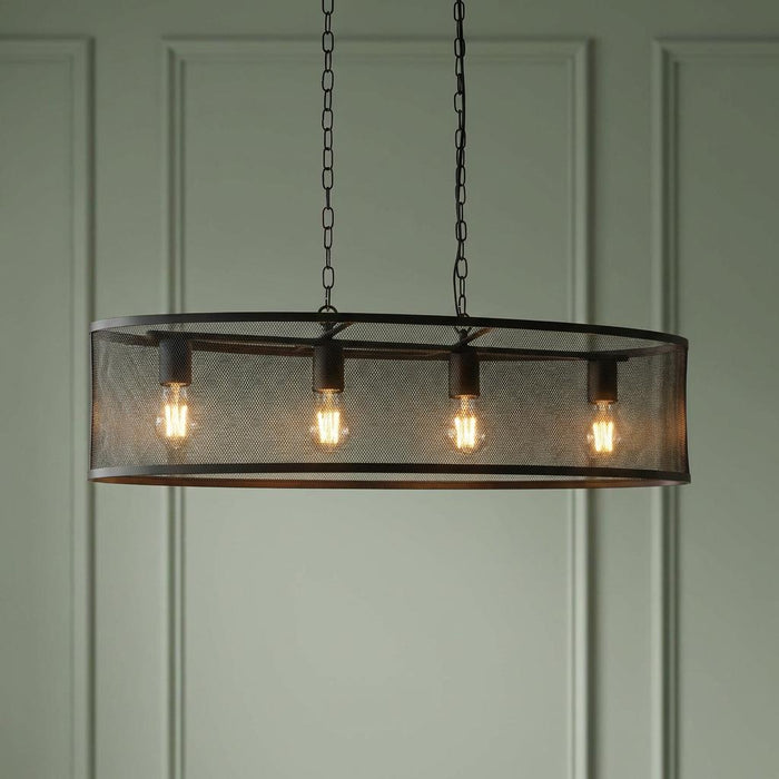 Four-light black mesh drum pendant with glowing bulbs suspended by chains in front of a green paneled wall.
