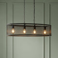 Four-light black mesh drum pendant with glowing bulbs suspended by chains in front of a green paneled wall.