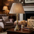 Flemish brass table lamp with a pleated mink shade on a wooden table in a cozy living room setting.