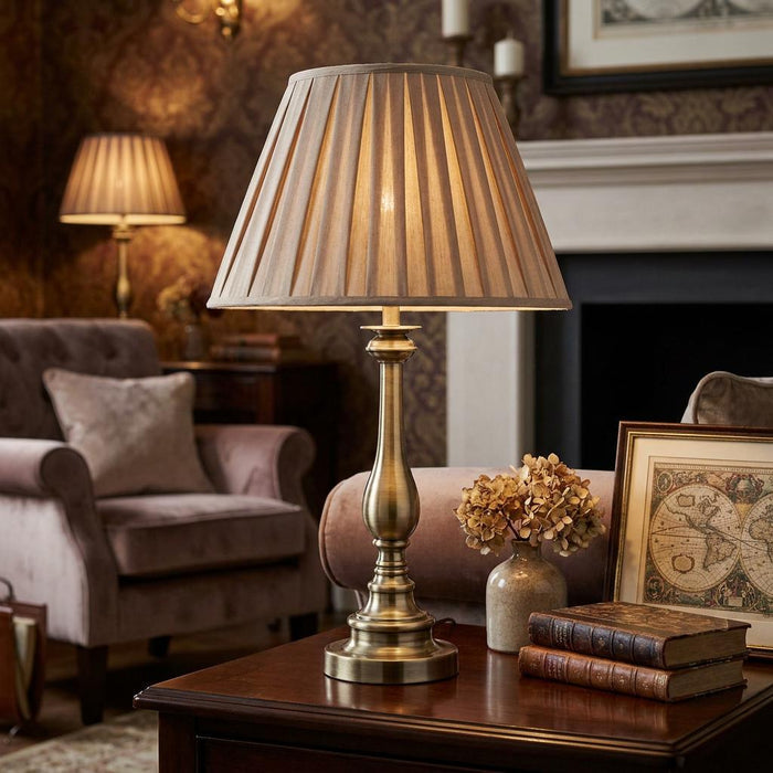 Flemish brass table lamp with a pleated mink shade on a wooden table in a cozy living room setting.