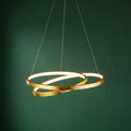 Two interlocking gold leaf rings form a modern LED pendant light glowing against a dark green textured background.