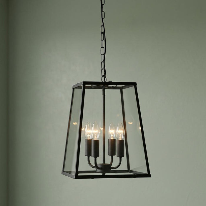 A black four-light lantern pendant with clear glass panels hanging against a pale green wall.