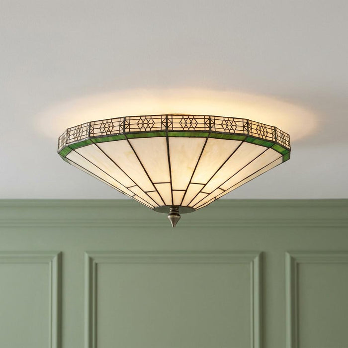 Illuminated flush Tiffany ceiling light with white and green geometric glass panels against a green paneled wall.